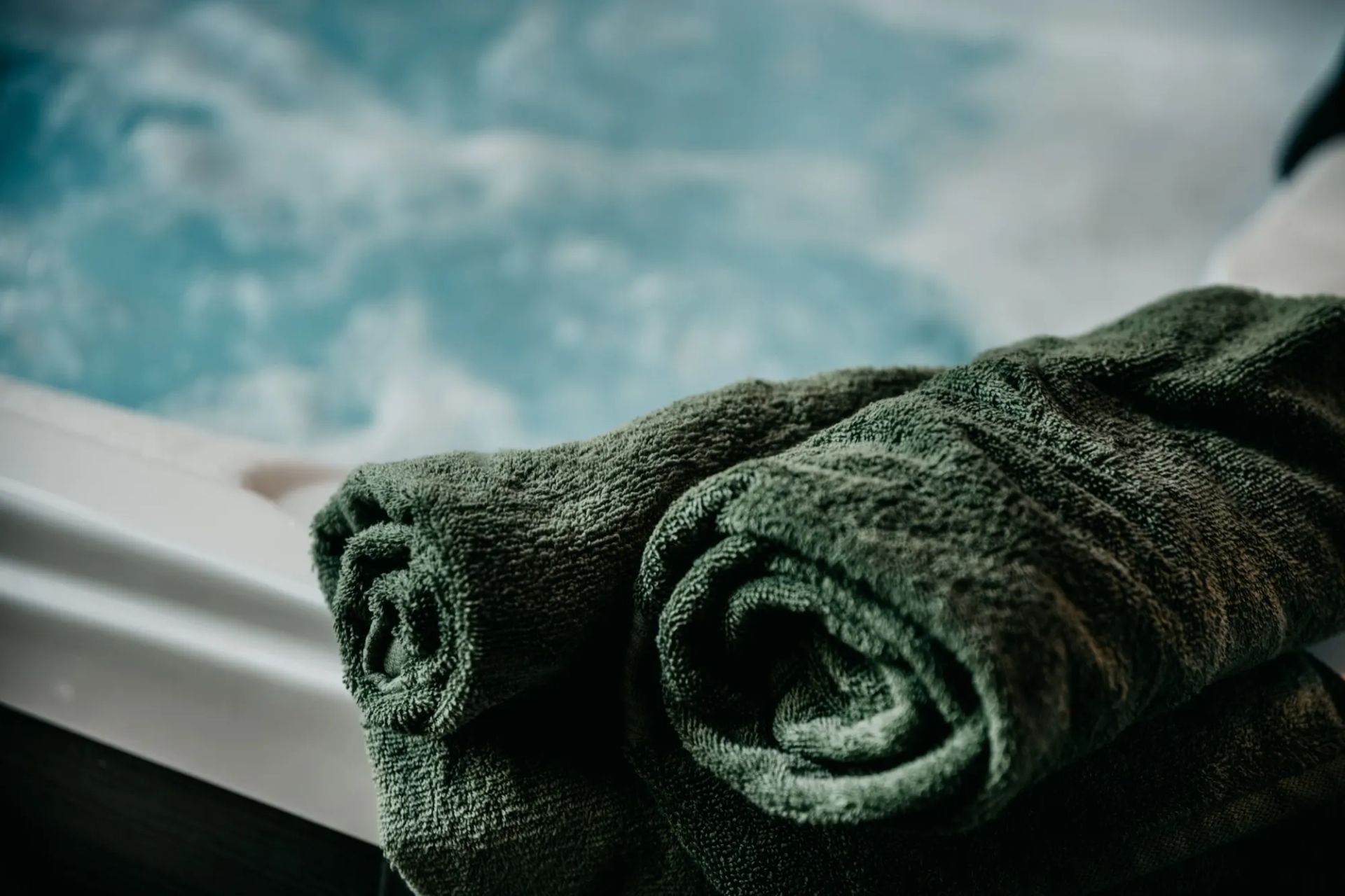 Feltekert zöld törölközők a pezsgő jakuzzi szélén